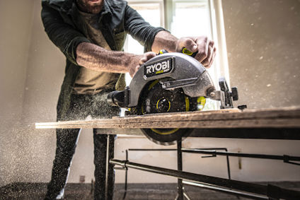 En person använder en Ryobi cirkelsåg för att såga genom en träplanka, med sågspån som flyger.
