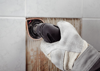 Hand i arbetshandske använder verktyg på kaklat vägg.