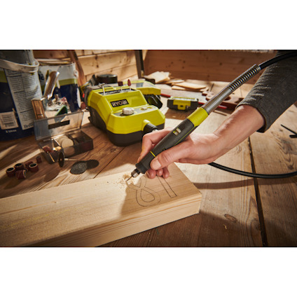 Hand gravera träbit med polerverktyg av märket RYOBI på arbetsbänk.