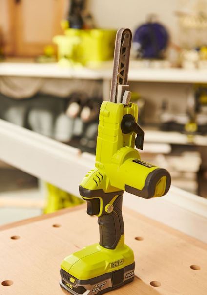 Grön batteridriven slipsåg placerad på en träyta i verkstadsmiljö.