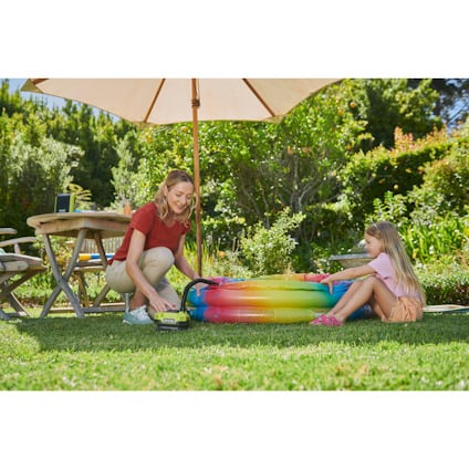 Kvinna och barn leker med en uppblåsbar pool i trädgården. Multikompressor från Ryobi syns i bild.