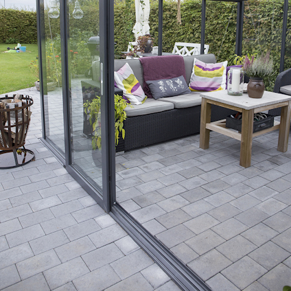 Utemöbler på inglasad veranda med kuddar, växter på bordet och trädgård i bakgrunden.