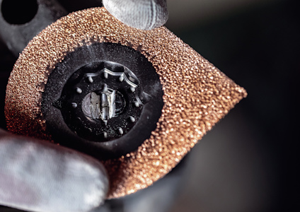 Närbild av en vinkelslip med rosafärgad skyddsplatta och handskklädd hand.