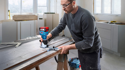 Person använder en eldriven handöverfräs på en träplanka i en verkstadsmiljö.